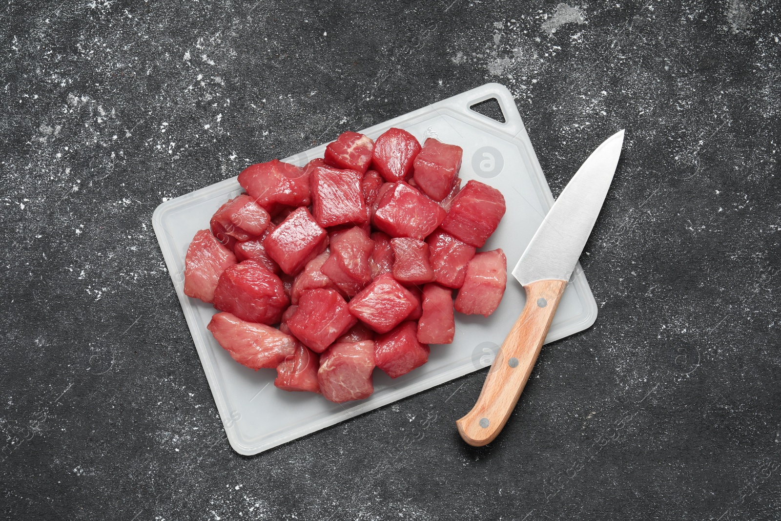 Photo of Cooking delicious goulash. Raw beef meat and knife on grey textured table, top view
