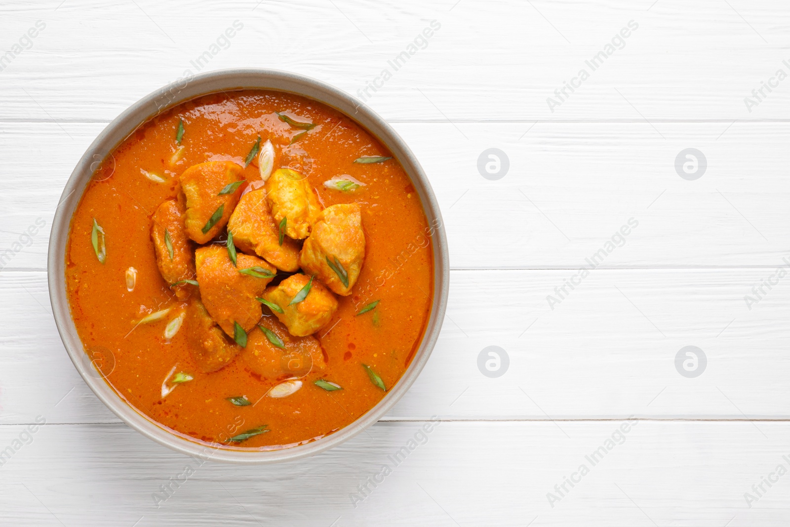 Photo of Bowl of delicious chicken curry on white wooden table, top view. Space for text