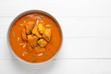 Photo of Bowl of delicious chicken curry on white wooden table, top view. Space for text