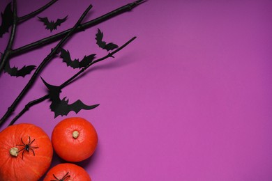 Flat lay composition with black branches, paper bats and pumpkins on purple background, space for text. Halloween celebration