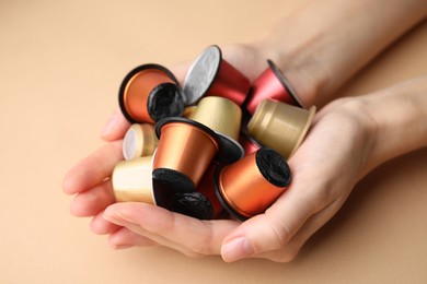 Woman holding heap of coffee capsules on beige background, closeup