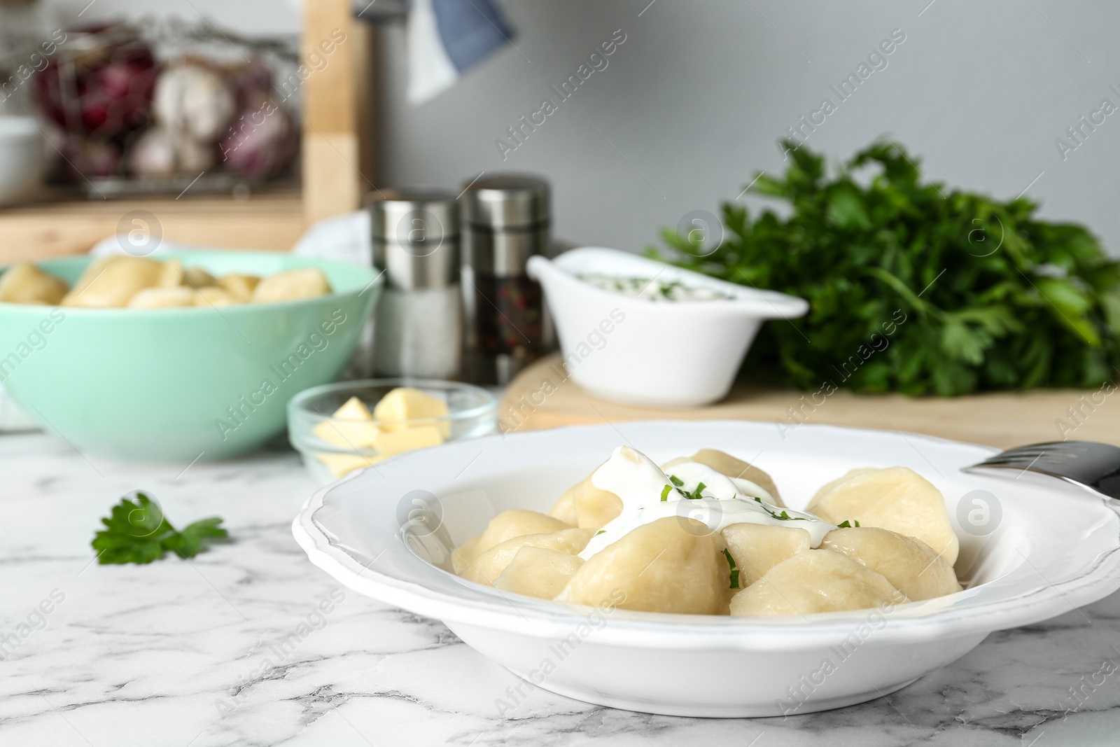 Photo of Delicious cooked dumplings with sour cream on white marble table