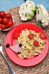 Photo of Creative serving for kids. Plate with cute hedgehog made of delicious pasta, sausages and tomatoes on light blue wooden table, flat lay