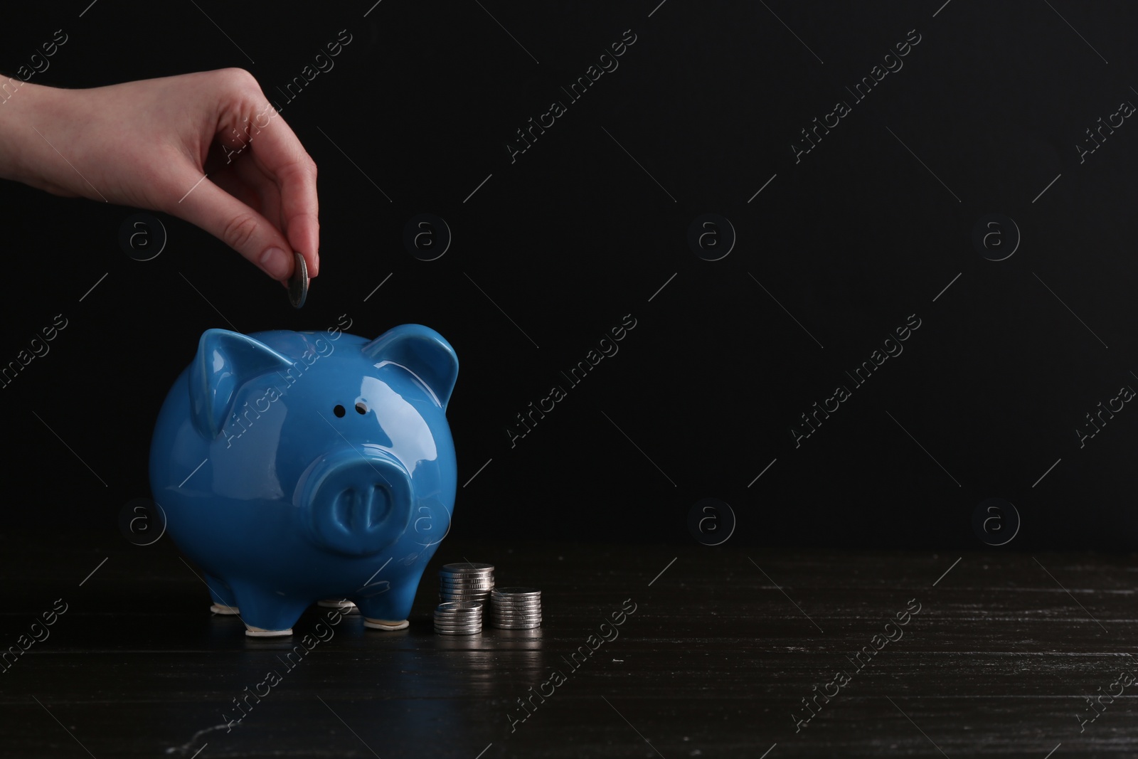 Photo of Financial savings. Woman putting coin into piggy bank at wooden table, closeup. Space for text