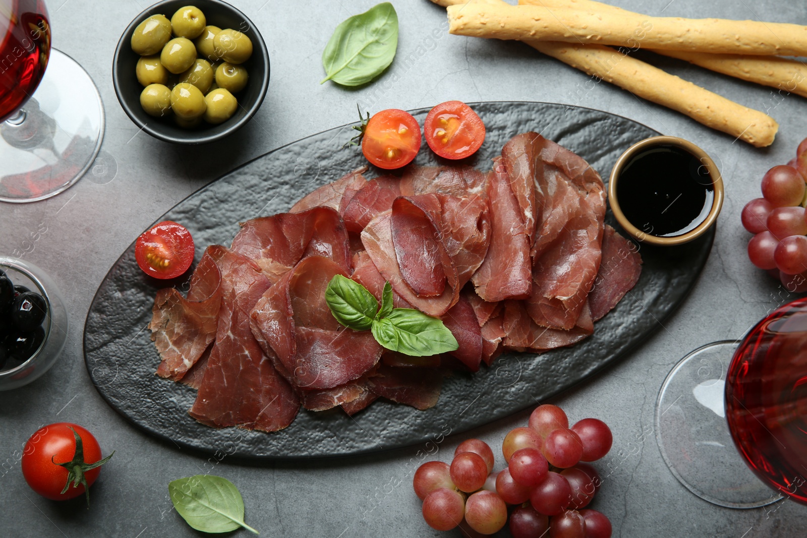 Photo of Delicious bresaola and different products served on grey textured table, flat lay