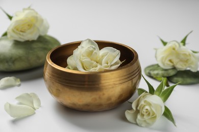 Photo of Tibetan singing bowl with water and beautiful rose flowers on white background, closeup
