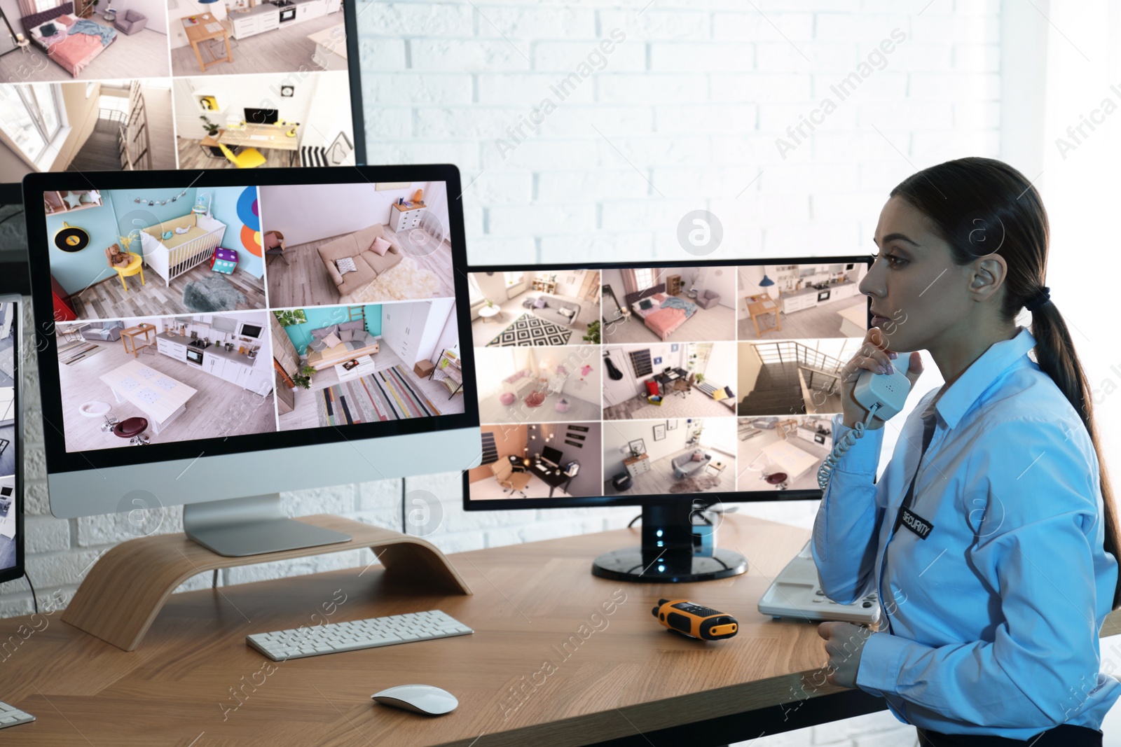 Photo of Female security guard talking by telephone near monitors at workplace