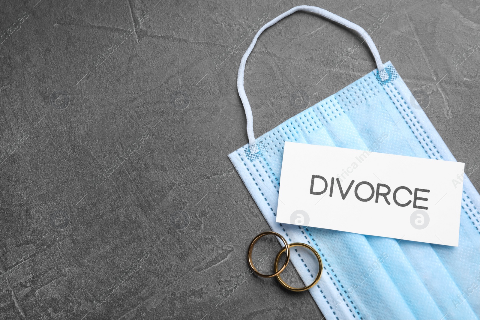 Photo of Flat lay composition protective mask and wedding rings on grey table, space for text. Divorce during coronavirus quarantine