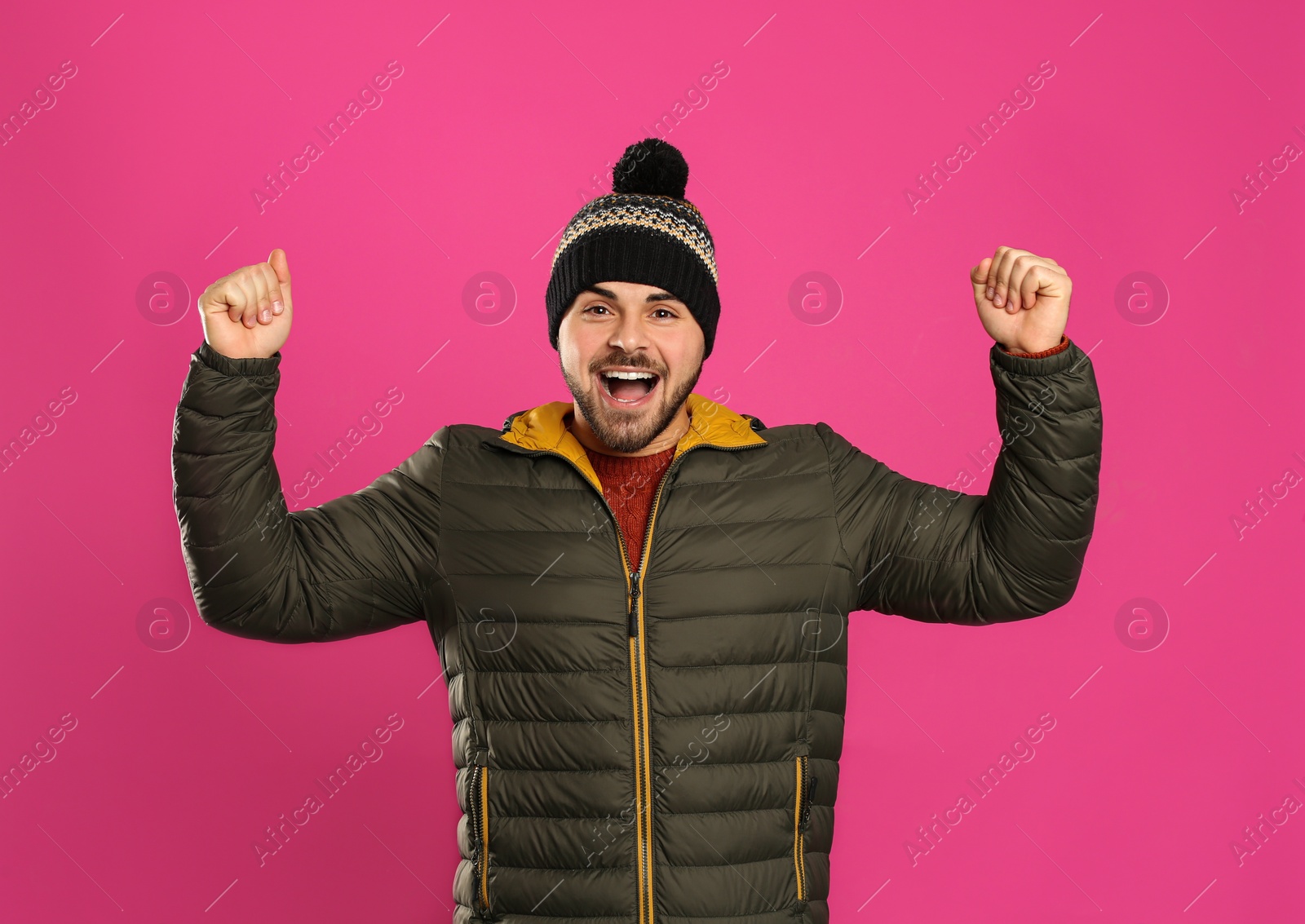 Photo of Happy young man in warm clothes on pink background. Winter vacation