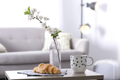 Photo of Fresh croissant, cup and flowers on table in room