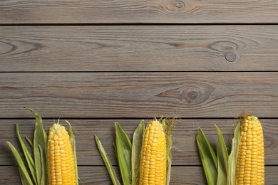 Tasty sweet corn cobs on wooden table, flat lay. Space for text