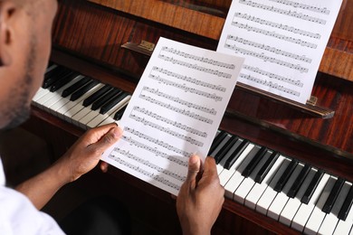 Photo of African-American man with note sheets at piano, closeup. Talented musician