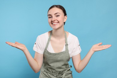 Beautiful young woman in clean apron with pattern on light blue background