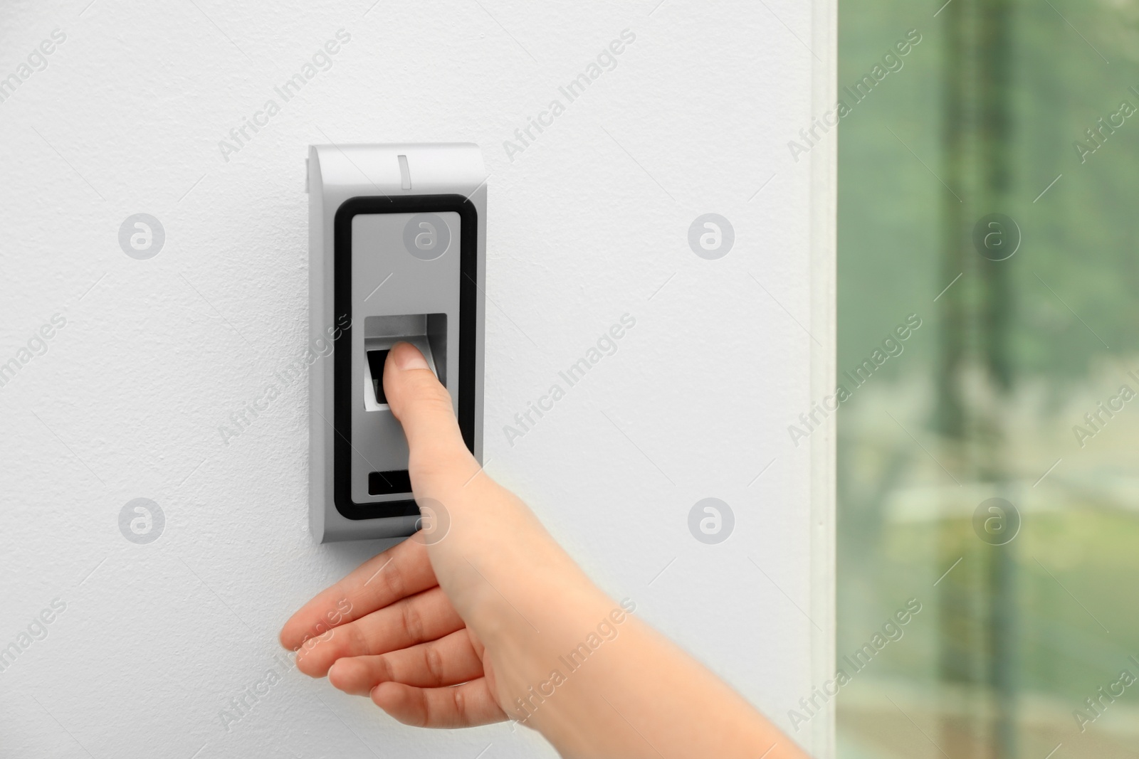 Photo of Young woman scanning fingerprint on alarm system indoors