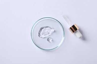 Photo of Petri dish with cosmetic serum and pipette on white background, flat lay