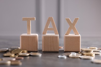 Photo of Word Tax, wooden letters and coins on grey table