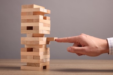 Photo of Playing Jenga. Man building tower with blocks at wooden table against grey background, closeup