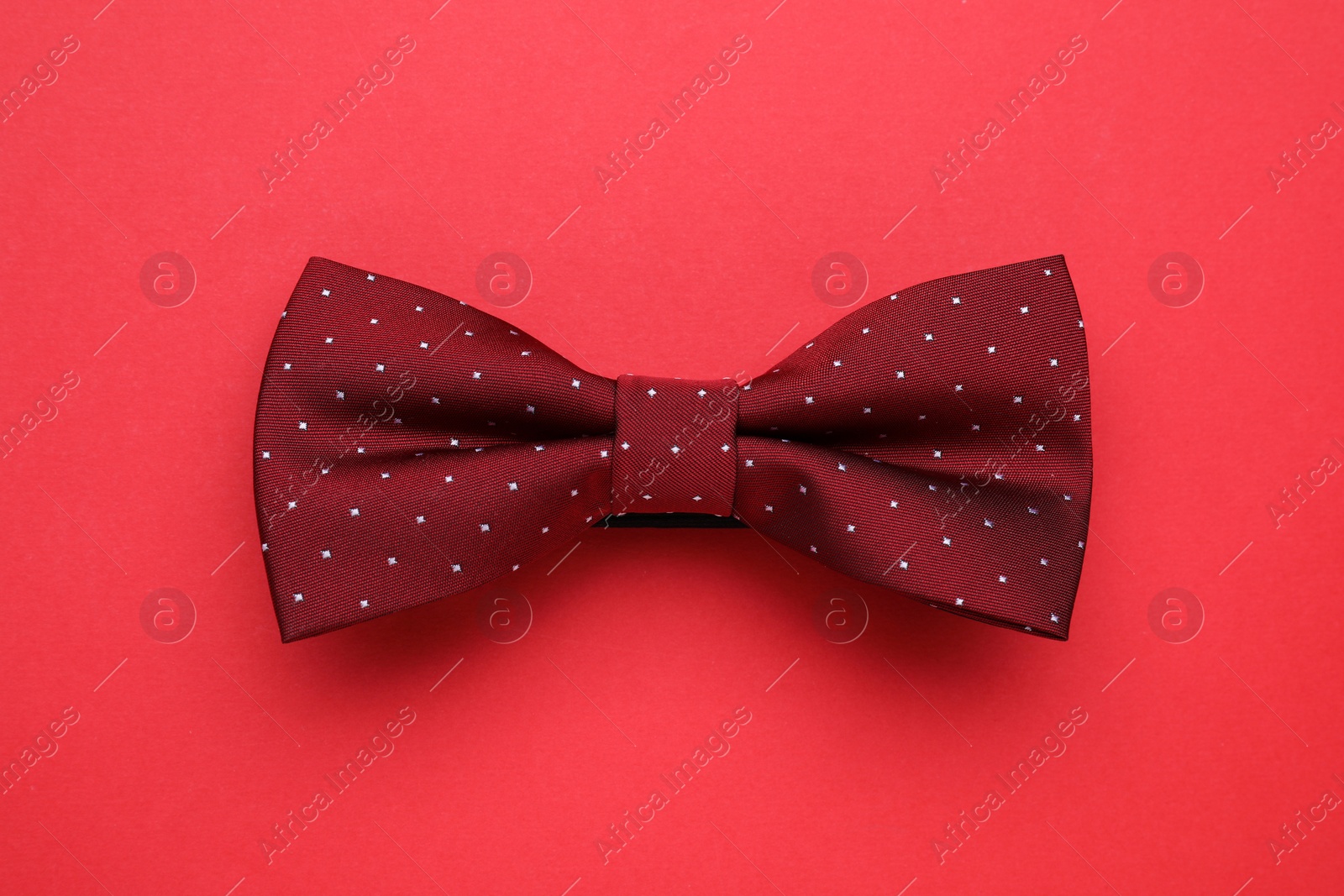 Photo of Stylish burgundy bow tie on red background, top view