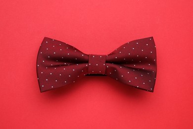 Stylish burgundy bow tie on red background, top view