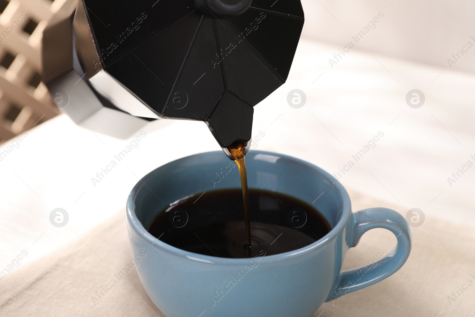 Photo of Pouring aromatic coffee from moka pot into cup at white table, closeup