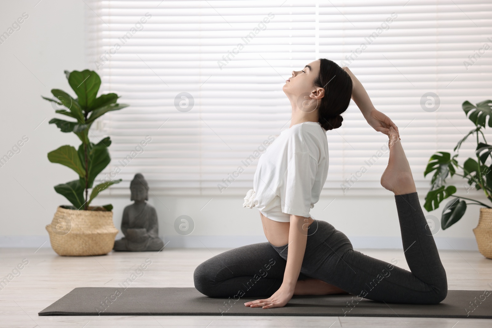 Photo of GIrl practicing one legged king pigeon asana on mat in yoga studio. Eka pada rajakapotasana pose