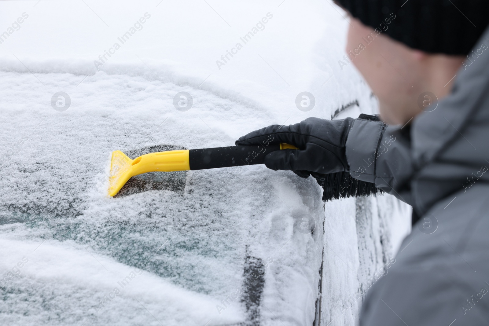 Photo of Man cleaning snow from car windshield outdoors, closeup