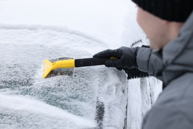 Photo of Man cleaning snow from car windshield outdoors, closeup