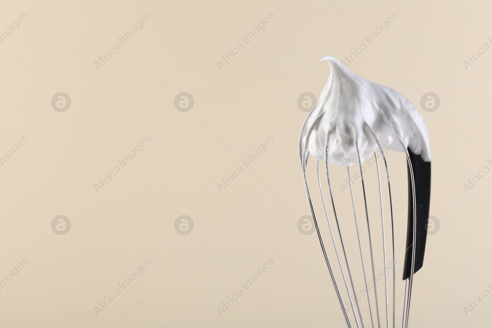 Photo of Whisk with whipped cream on beige background, closeup. Space for text