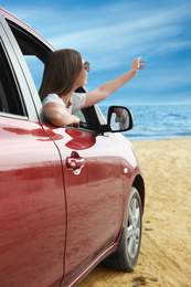 Photo of Happy woman leaning out of car window on beach. Summer vacation trip