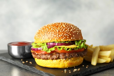 Photo of Burger with delicious patty, french fries and sauce on dark table against gray background, closeup