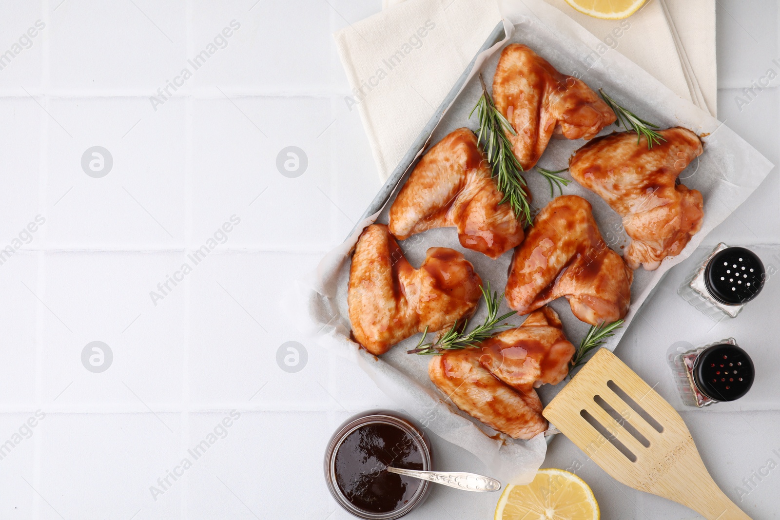 Photo of Raw chicken wings, rosemary, marinade and spices on light tiled table, flat lay. Space for text