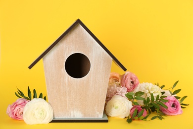 Photo of Stylish bird house and fresh eustomas on yellow background