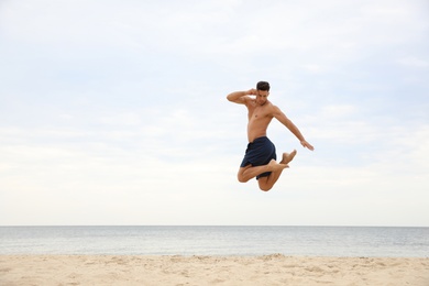 Photo of Muscular man jumping on beach, space for text. Body training