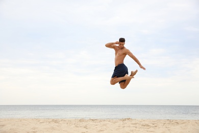 Muscular man jumping on beach, space for text. Body training