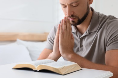 Photo of Religious man with Bible praying in bedroom, closeup