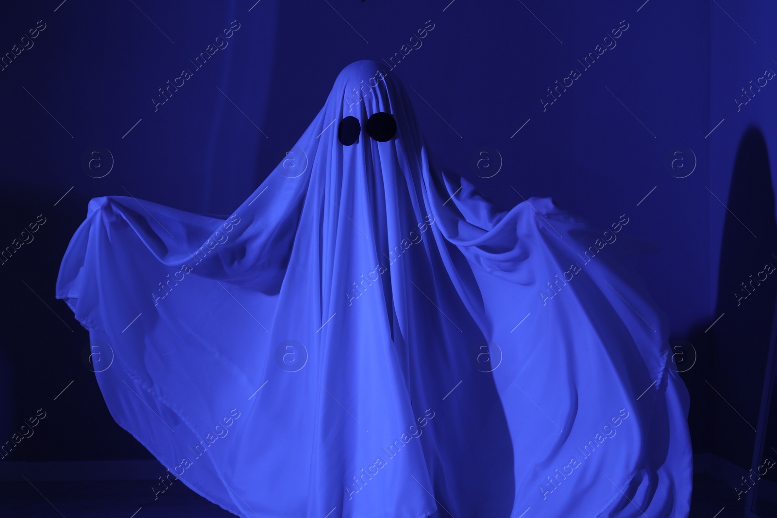 Photo of Creepy ghost. Woman covered with sheet in blue light