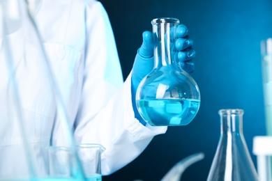 Photo of Scientist holding Florence flask with liquid on color background, closeup. Solution chemistry