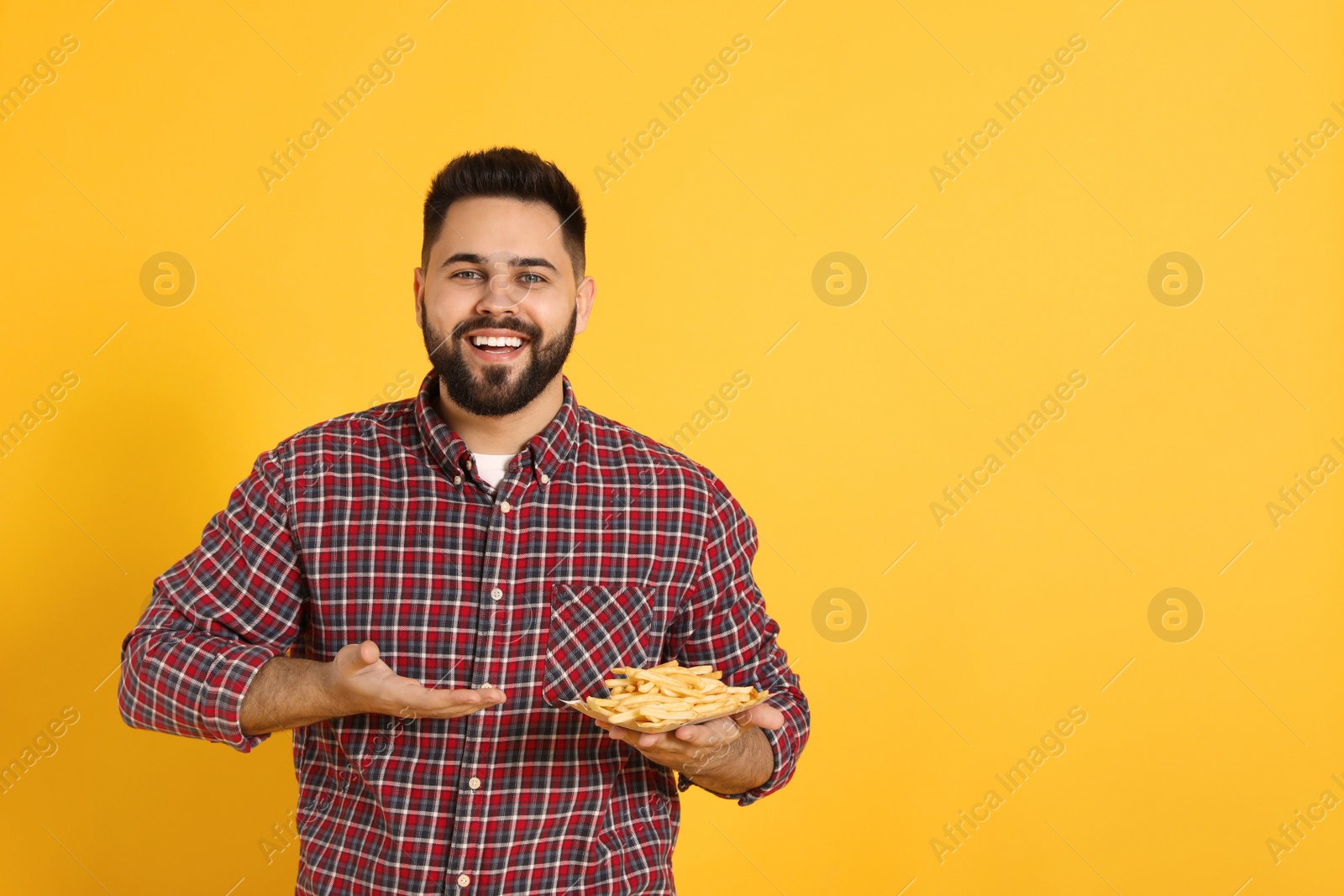 Photo of Young man with French fries on orange background, space for text