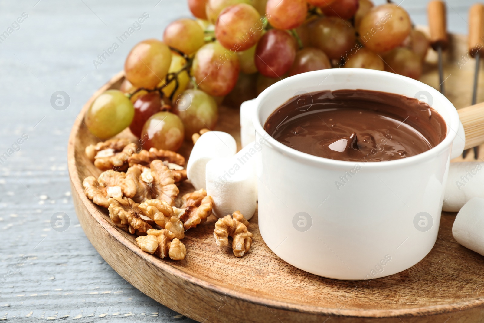 Photo of Fondue pot with milk chocolate and products on grey wooden table, closeup