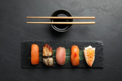 Serving board with delicious nigiri sushi and soy sauce on black table, flat lay