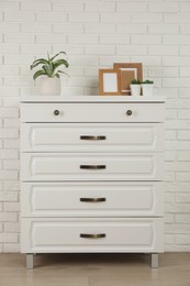 Photo of Modern chest of drawers with decor near white brick wall