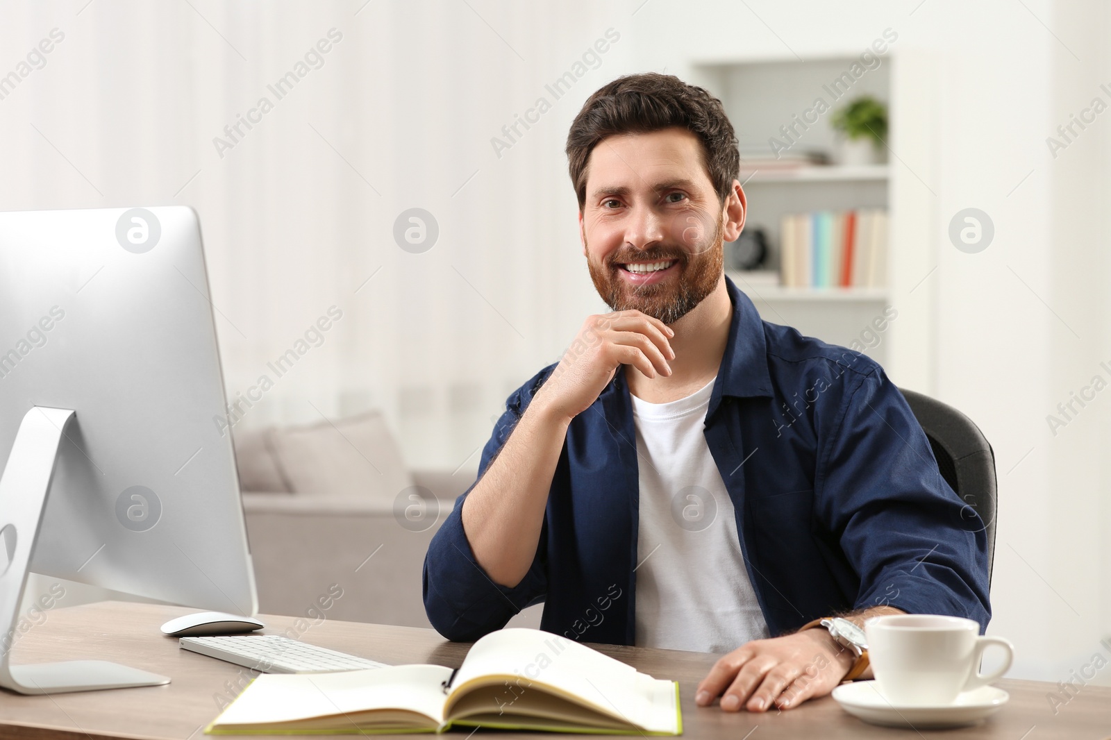 Photo of Home workplace. Happy man at wooden desk with computer in room