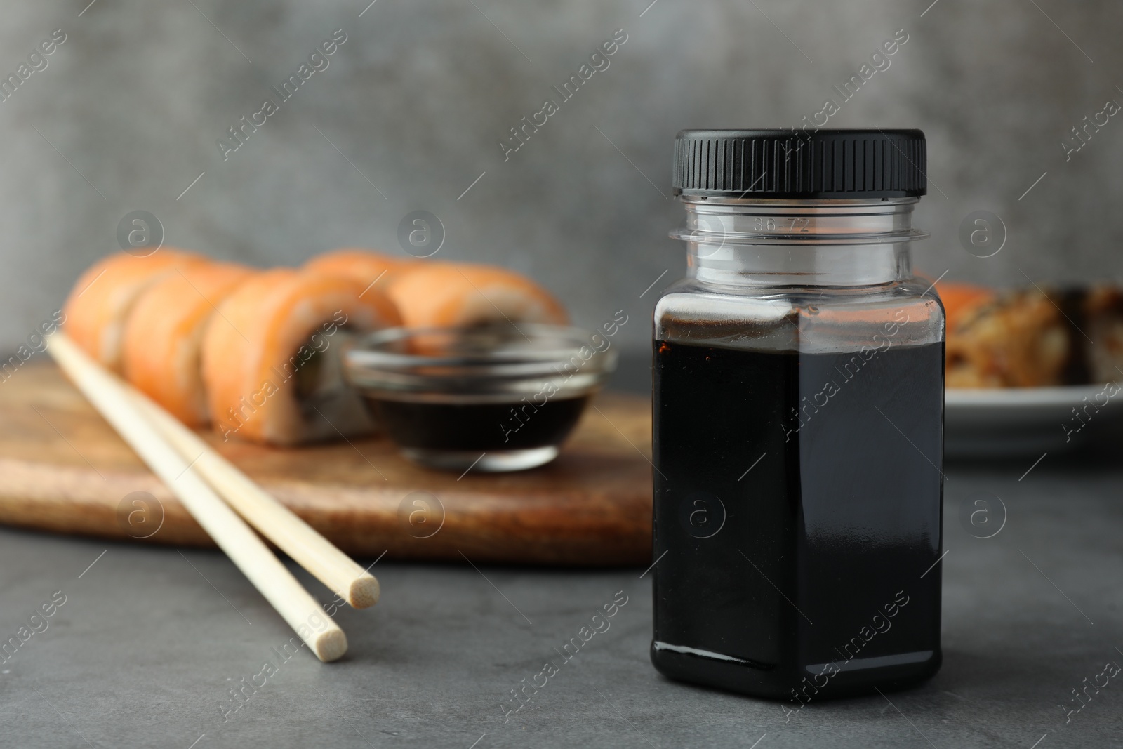 Photo of Tasty soy sauce, chopsticks and sushi rolls with salmon on grey table. Space for text