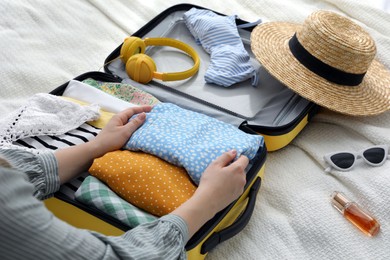 Woman packing suitcase for trip on bed, closeup