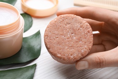 Woman holding solid shampoo bar at light wooden table, closeup. Hair care