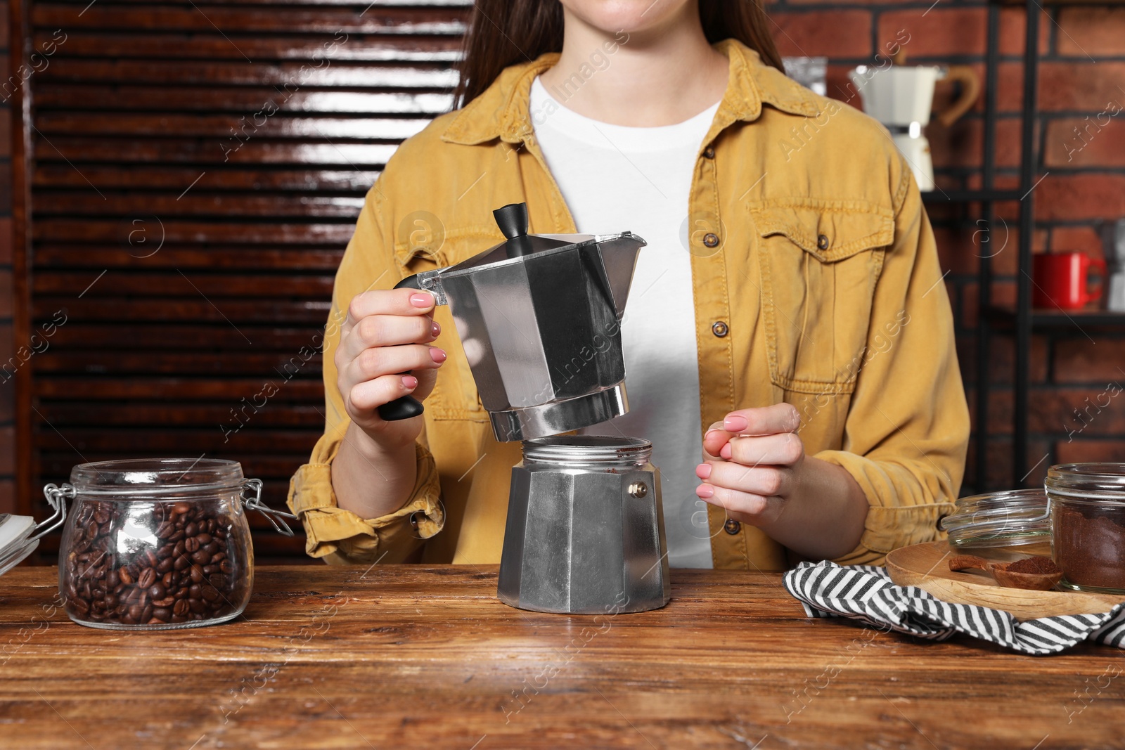 Photo of Woman making coffee in moka pot at wooden table, closeup