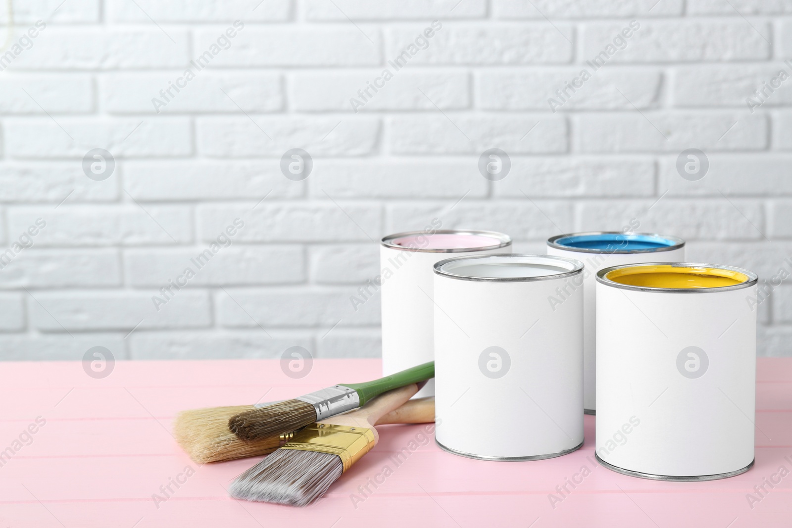 Photo of Cans of colorful paints and brushes on pink wooden table. Space for text