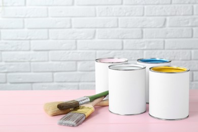 Photo of Cans of colorful paints and brushes on pink wooden table. Space for text