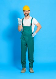 Photo of Professional repairman in uniform with smartphone on light blue background