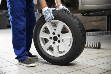 Mechanic with car tire in service center, closeup